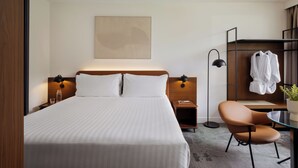 Habitació d'hotel amb llit, taules de nit, una cadira, un armari i una obra d'art penjada a la paret.