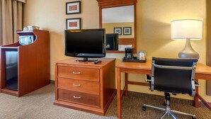 A hotel room with a wooden desk, a television, a chair, a dresser, and a mirror. - Quality Inn Pueblo North (Pueblo)