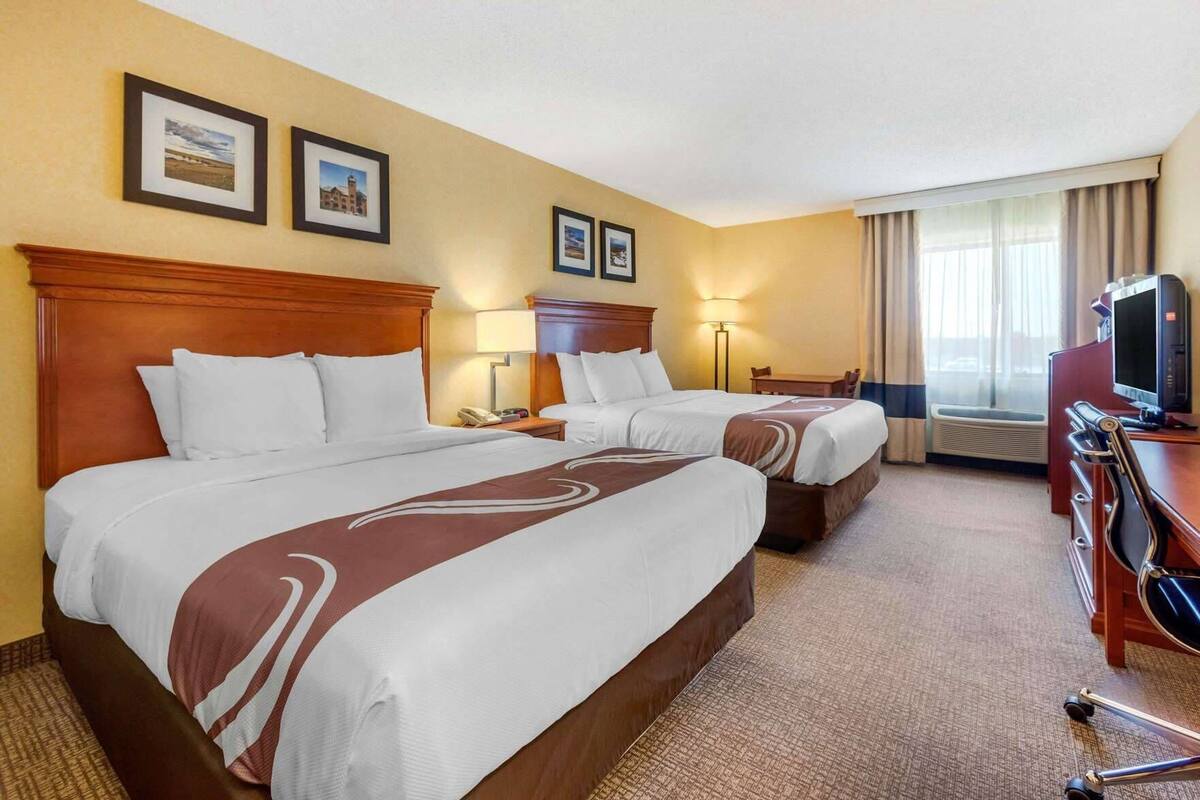 A hotel room with two beds, a desk, a TV, and a window with curtains.