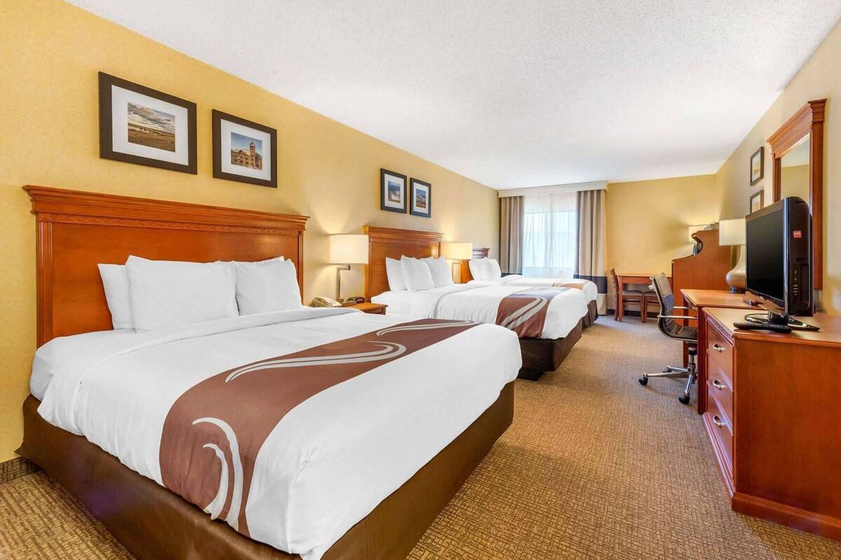 A hotel room with two beds, a desk, a chair, a TV, and framed pictures on the wall.