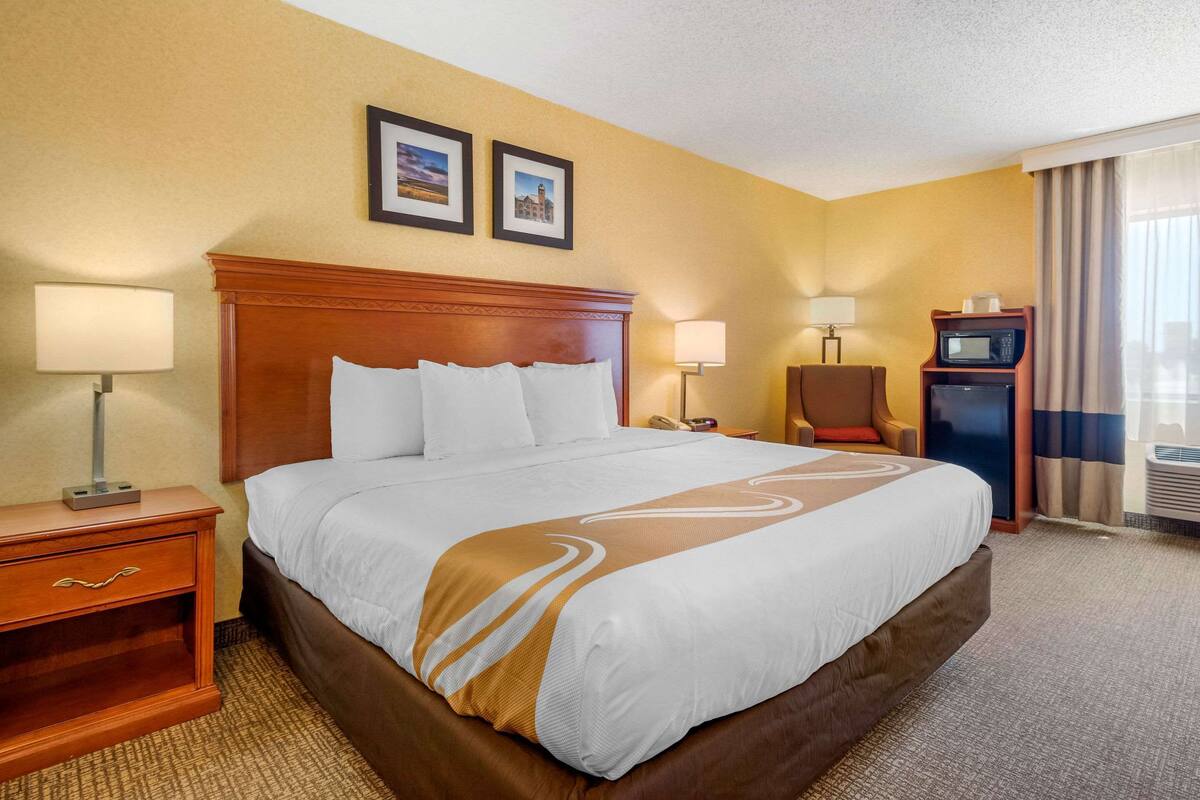 A hotel room with a large bed, two bedside lamps, a nightstand, a desk with a telephone, a microwave, and a picture frame on the wall.