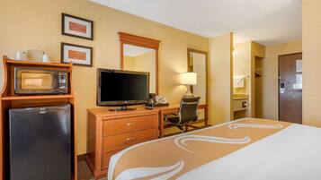 Habitación de hotel con cama, escritorio, computadora, microondas y refrigerador.