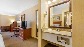 A hotel room with a bed, desk, chair, TV, and a bathroom with a sink, mirror, and towel rack. - Quality Inn Pueblo North (Pueblo)