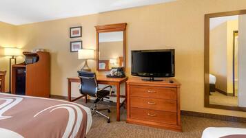 Une chambre d’hôtel comprenant un lit, un bureau, une chaise, une télévision, une commode et un grand miroir.