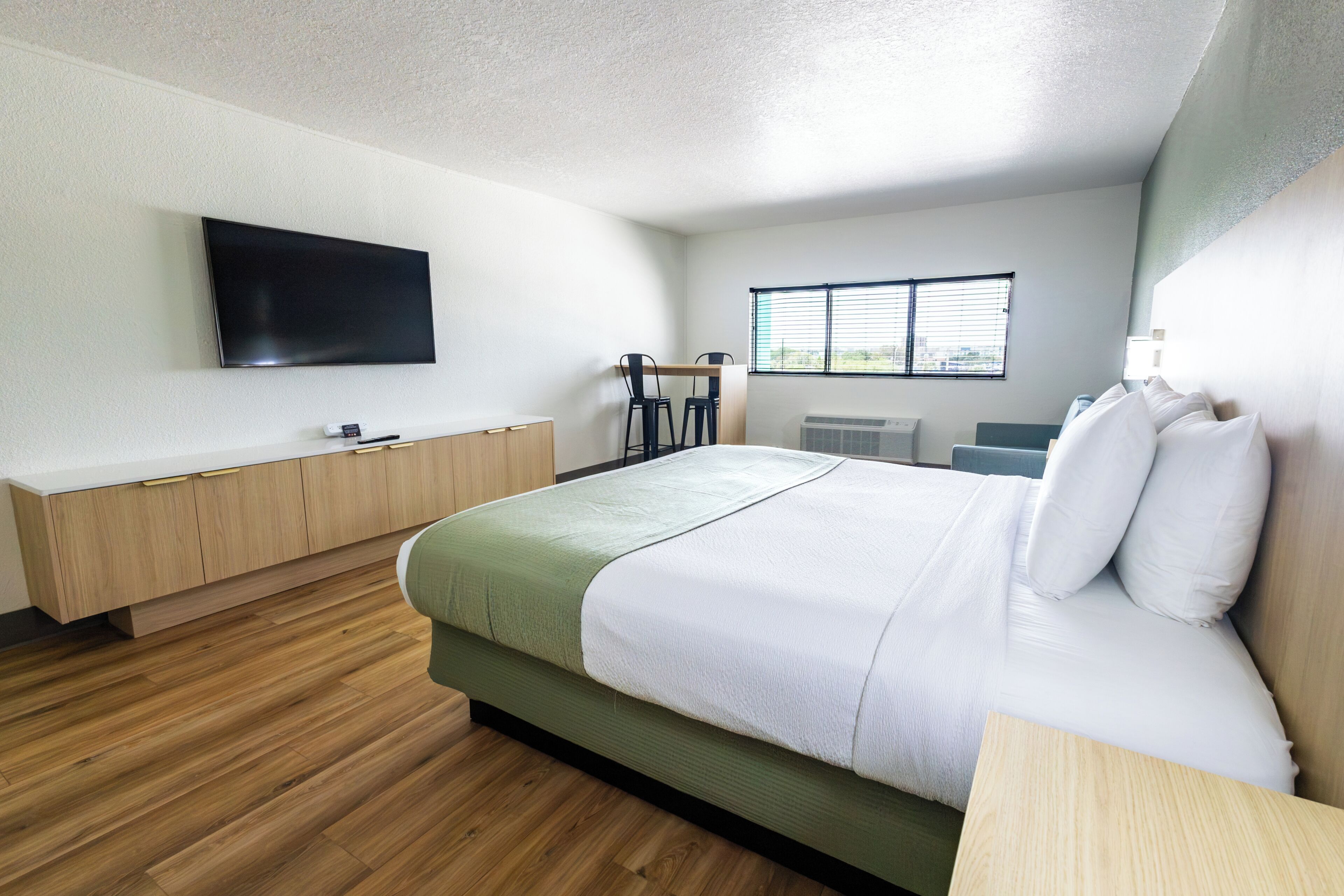 A modern hotel room with a bed, a TV, a desk, and a window.