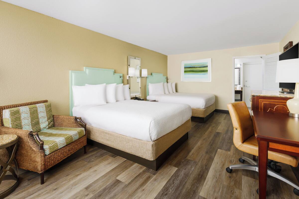 Quarto de hotel com uma cama grande, uma cama menor, um sofá, uma escrivaninha e uma cadeira.