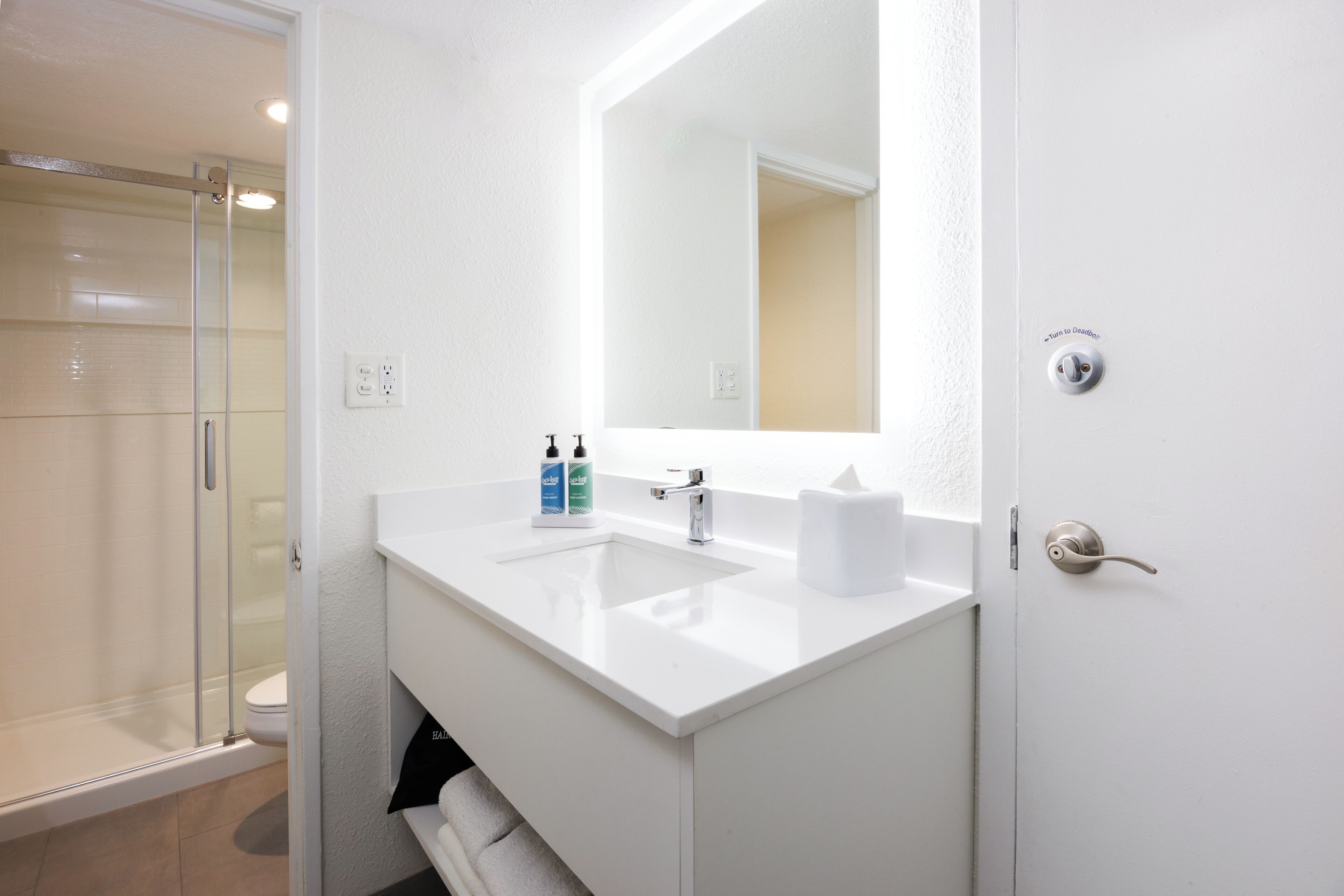Ein Badezimmer mit Glasdusche, einem weißen Waschbecken mit Spiegel und einem Handtuchhalter.