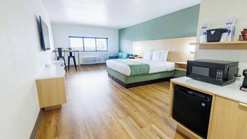 Una habitación de hotel moderna con cama, escritorio, microondas y lavavajillas.