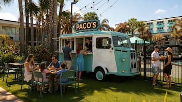 Un camión de comida llamado 'PACO'S' estacionado en un área con césped, donde personas están comiendo y paseando.