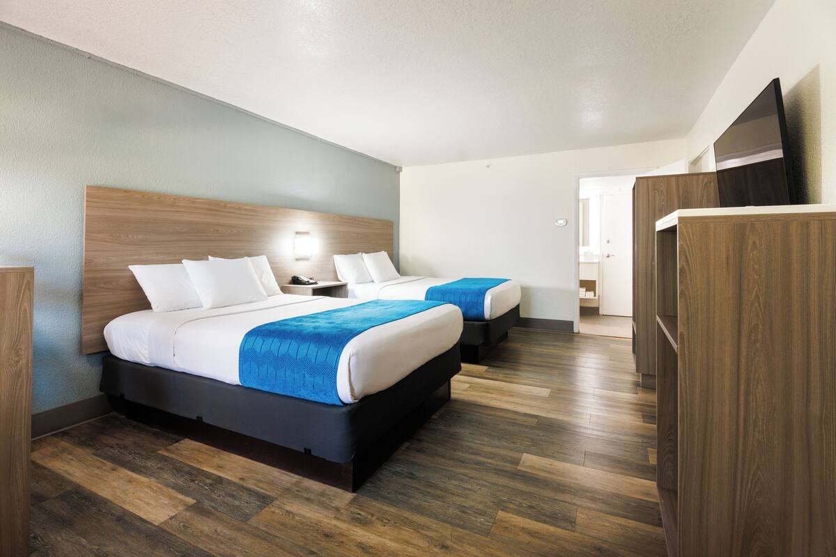Quarto de hotel com duas camas, cabeceiras de madeira e design moderno.