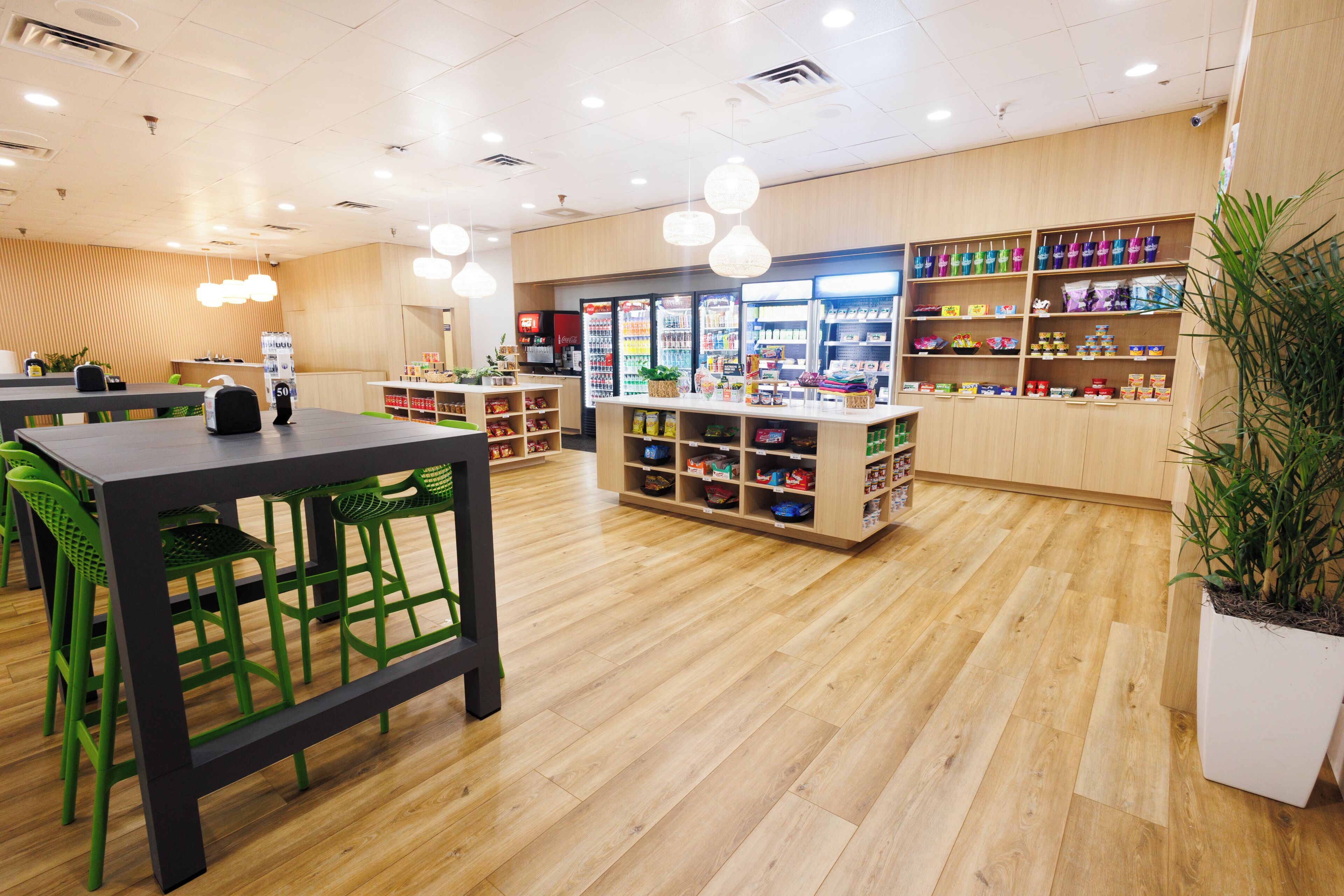 A clean, well-lit indoor space with wooden flooring, green chairs, a central counter with various items, and shelves stocked with products.