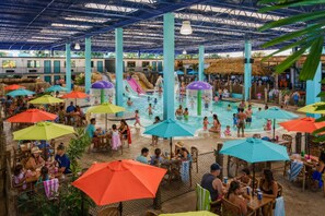 An indoor swimming pool area with multiple water slides, seating areas with umbrellas, and a covered dining section.