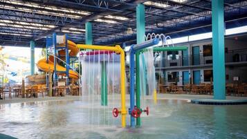 An indoor water park with a water slide, multiple water play structures, and seating areas.
