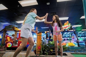 Two people high-fiving in an indoor play area with various arcade games and rides.