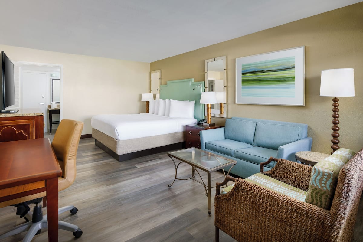 Quarto de hotel com cama, sofá, televisão, secretária e candeeiro.