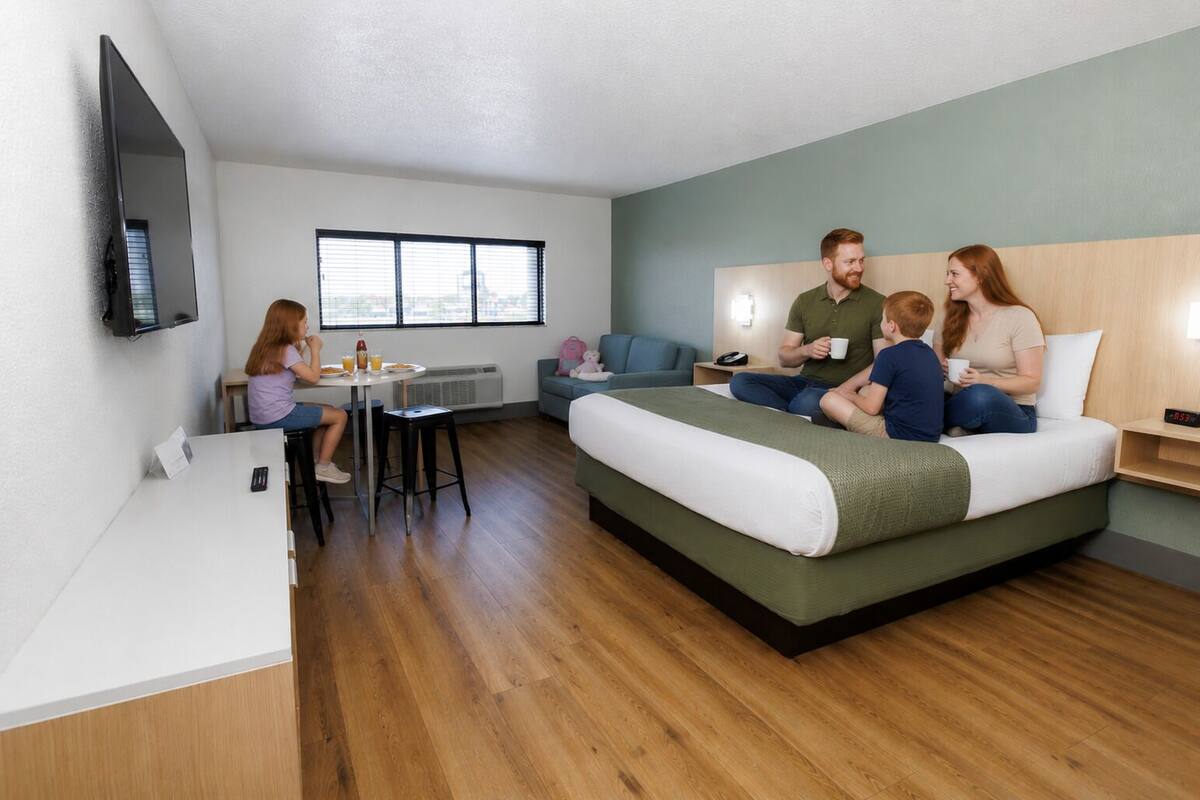 Quarto de hotel moderno com cama, mesa de jantar, televisão e janela.