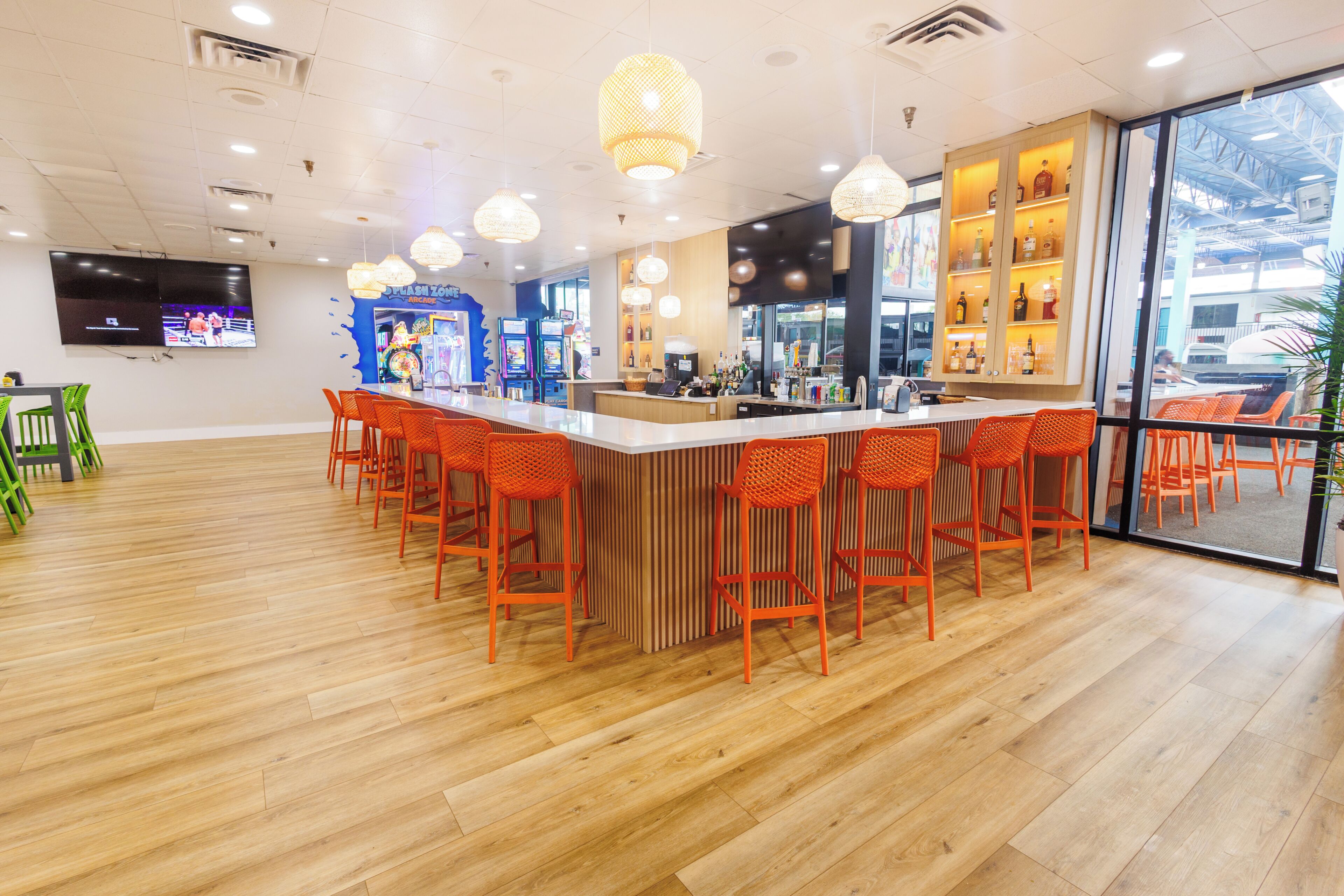 Un espace bar moderne avec un plancher en bois, des tabourets de bar orange et un téléviseur fixé au mur.