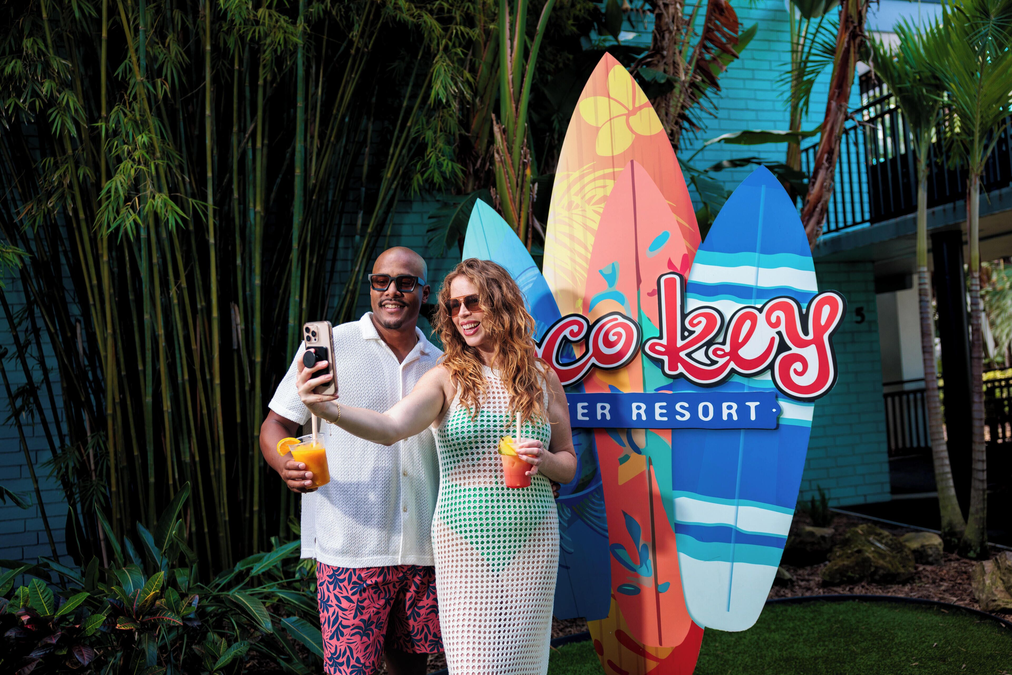 Una pareja se toma un selfie con tablas de surf frente al resort Coco Key Resort.