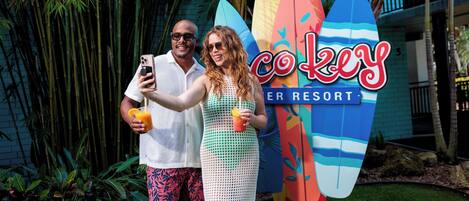 Una pareja se toma un selfie con tablas de surf frente al resort Coco Key Resort.