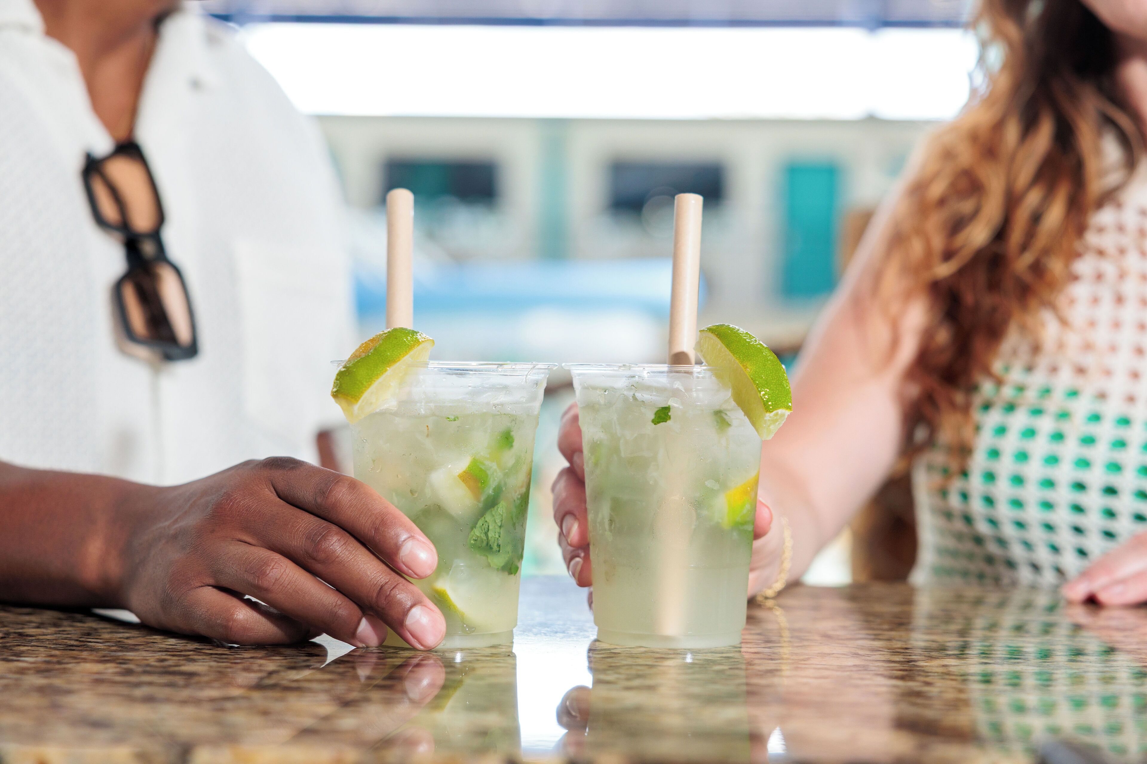 Two people holding glasses of a lime-based drink at a bar.