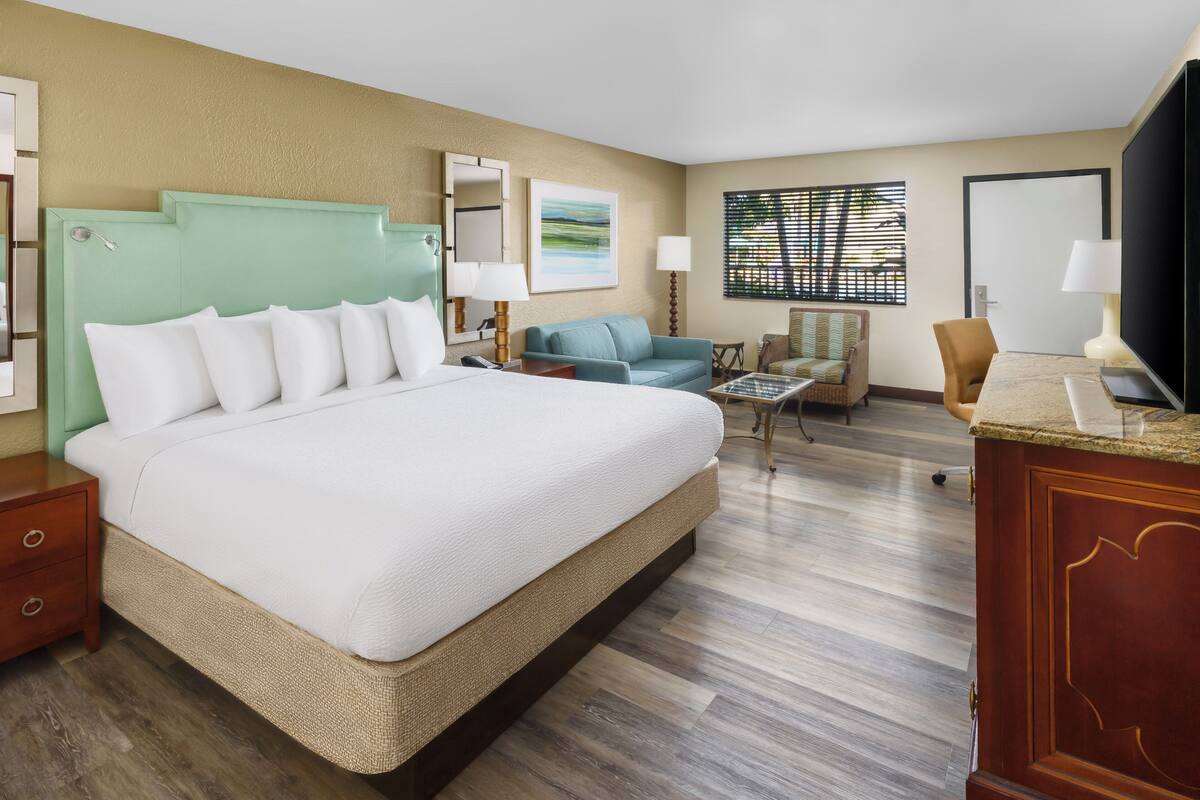 Quarto de hotel com uma cama grande, um sofá, uma cadeira, uma escrivaninha e uma televisão.