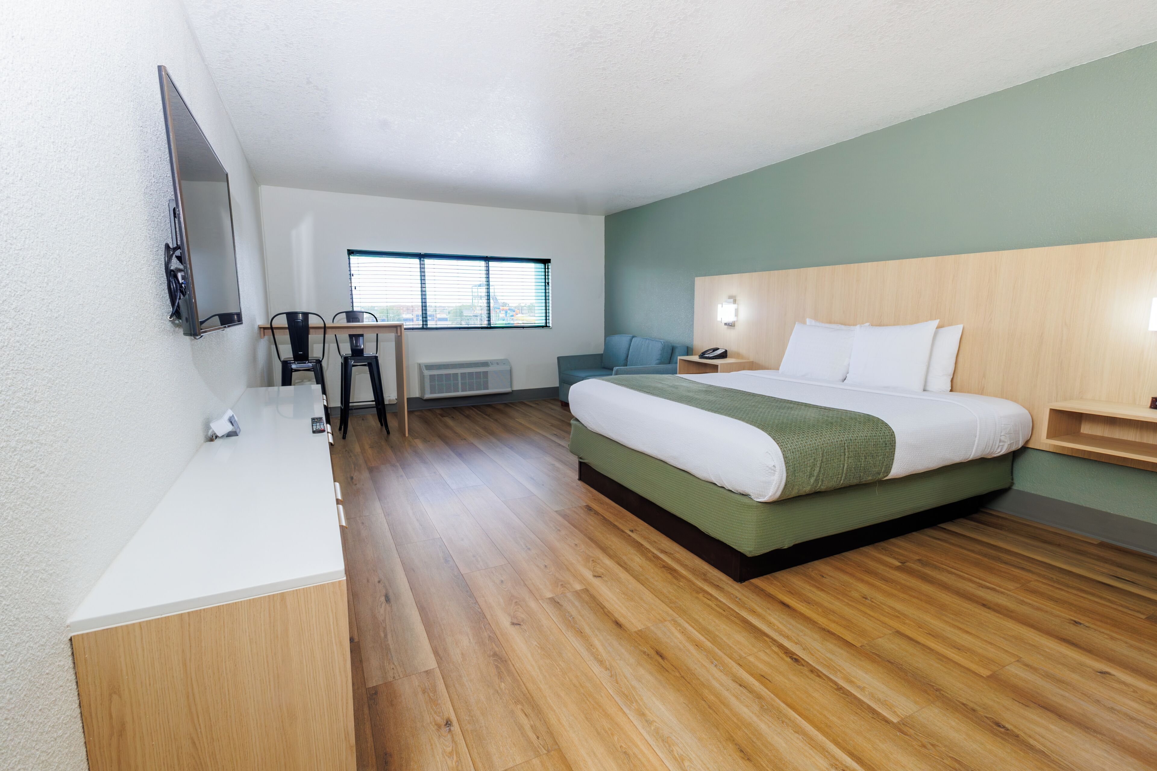 A modern hotel room with a large bed, a desk, a chair, a flat-screen TV, and a window with blinds.