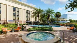 Zona de piscina de hotel con jacuzzi, sillas de descanso y palmeras.