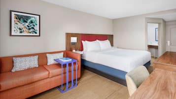 Una habitación de hotel con cama, sofá, una mesita y un cuadro en la pared.