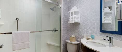 Un baño moderno con ducha envuelta en vidrio, un inodoro blanco y un mueble de tocador con espejo.