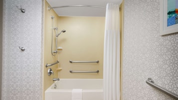 A modern bathroom with a bathtub, shower, and handrails.