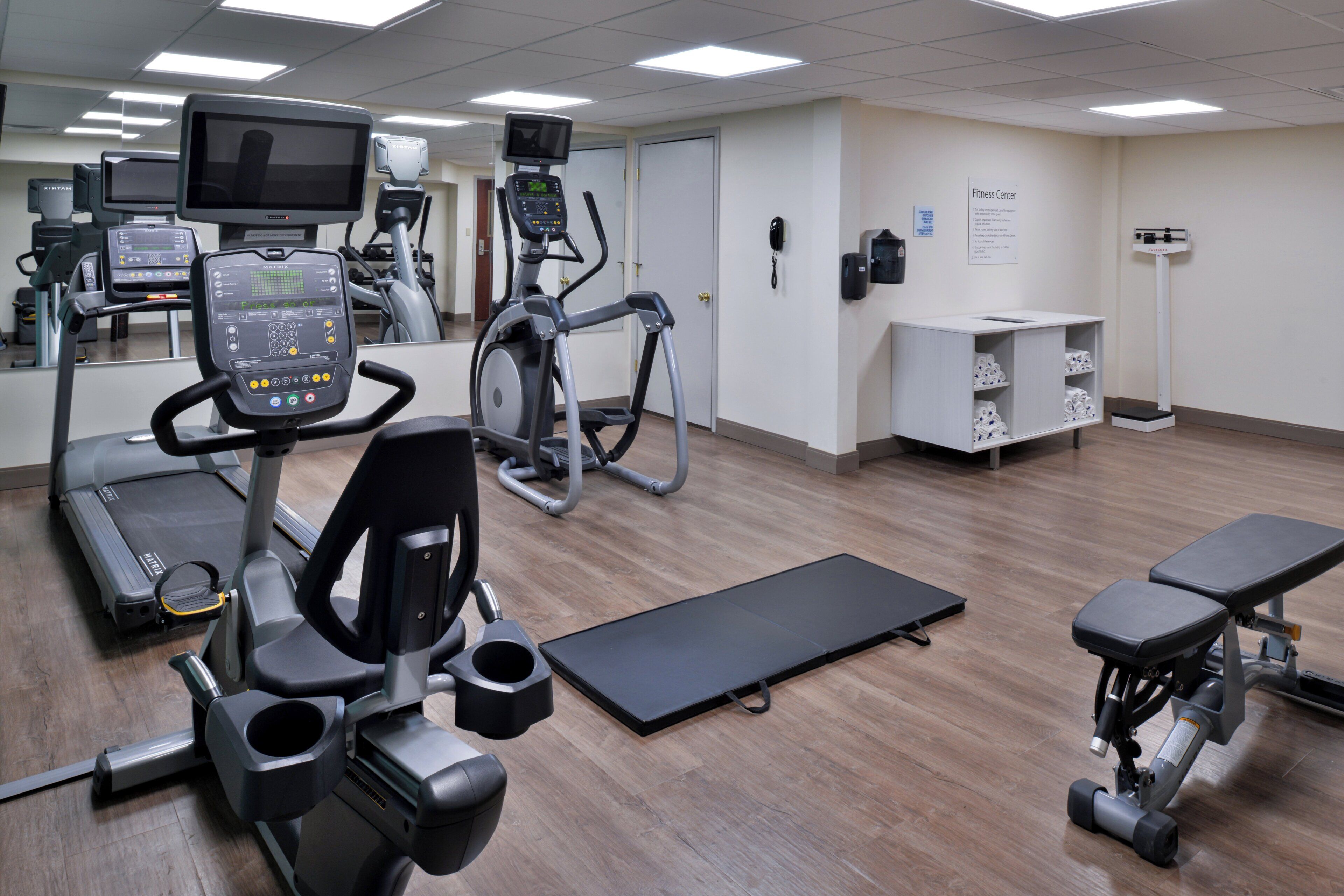 Une salle de sport équipée de tapis de course, de vélos elliptiques et d’un banc de musculation.