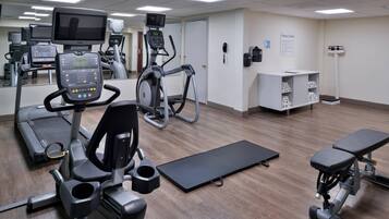 Une salle de sport équipée de tapis de course, de vélos elliptiques et d’un banc de musculation.