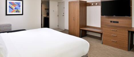 A hotel room with a large bed, a desk, a television, and a wardrobe.