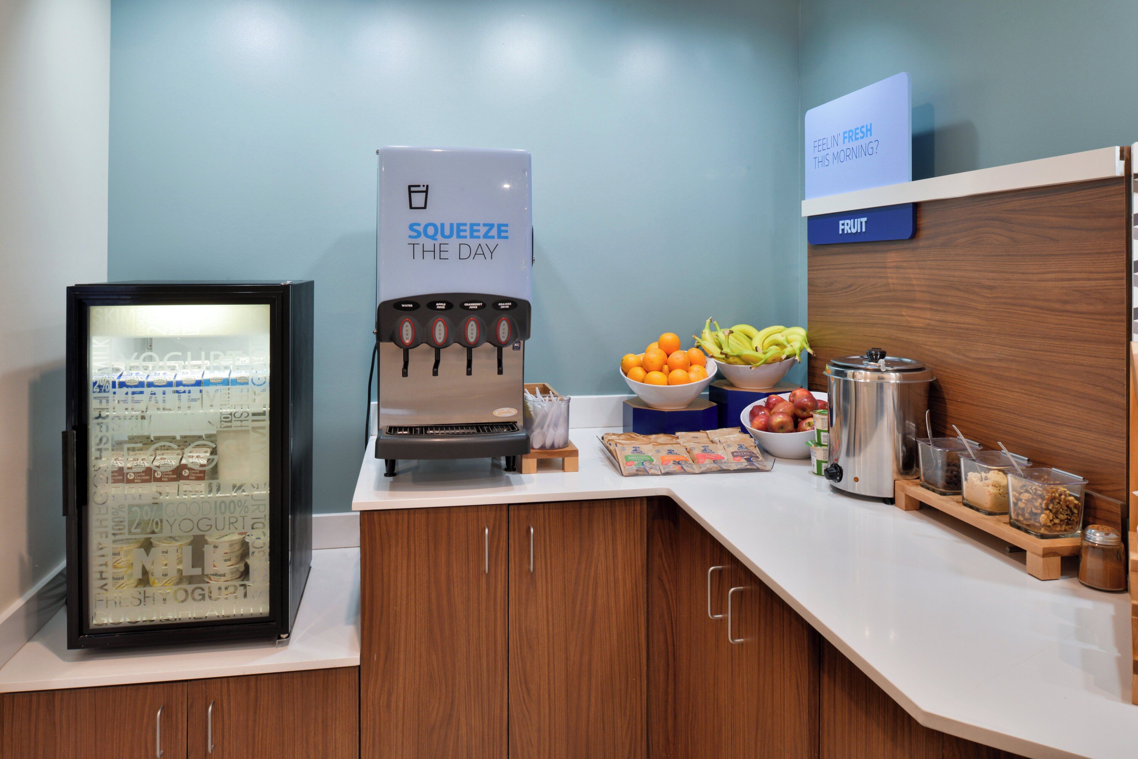 Estación de desayuno autoservicio con refrigerador, dispensador de bebidas y diversas opciones de comida.