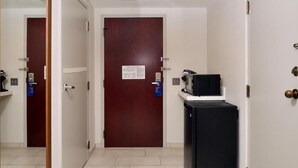 A hallway with a closed door, a black refrigerator, and a small table with a lamp. - Holiday Inn Express Blowing Rock South by IHG (Blowing Rock)