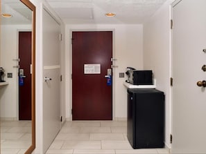 A hallway with a closed door, a black refrigerator, and a small table with a lamp.