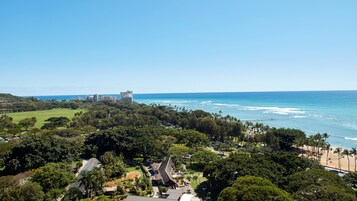 A coastal area with a beach, dense greenery, and a large building in the distance.
