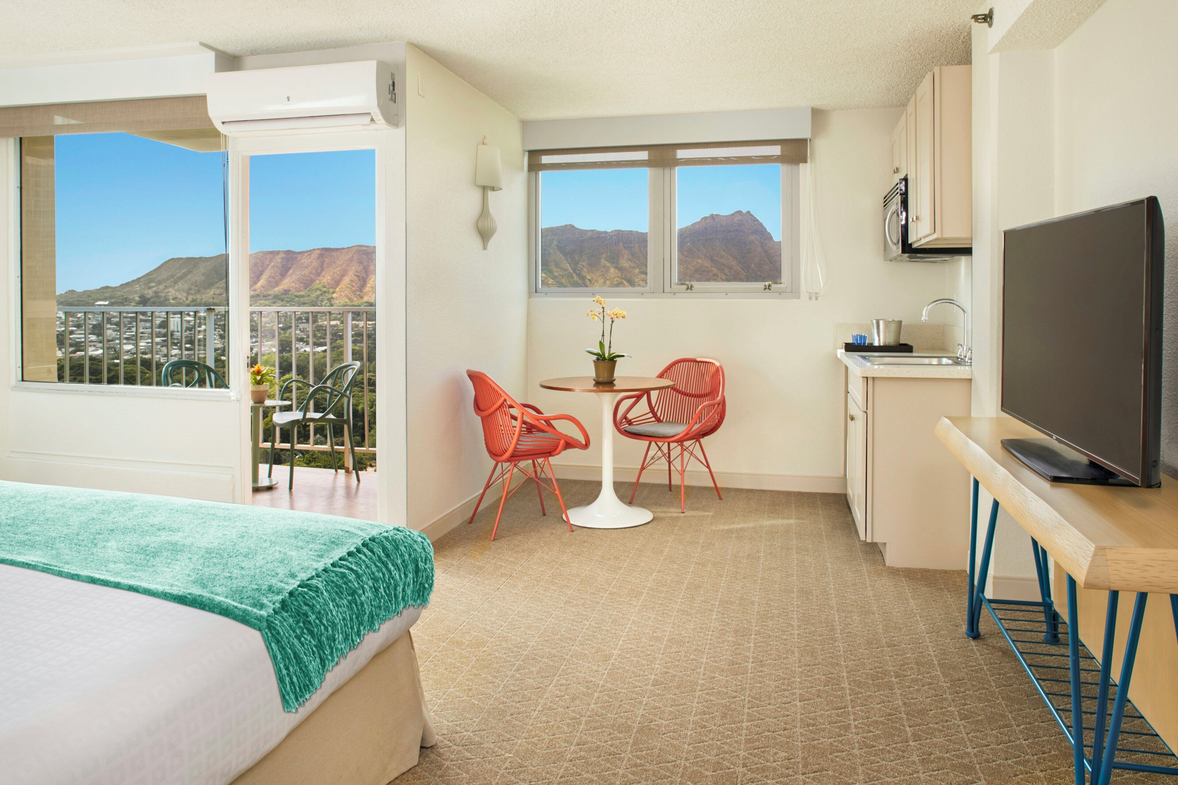 Una habitación de hotel con cama, un balcón con vistas, una zona de comedor con sillas, una mesa, un televisor y una cocina.