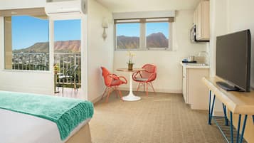 Una habitación de hotel con cama, un balcón con vistas, una zona de comedor con sillas, una mesa, un televisor y una cocina.