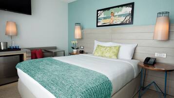 A hotel room with a bed, bedside table, lamp, artwork, and a TV mounted on the wall.