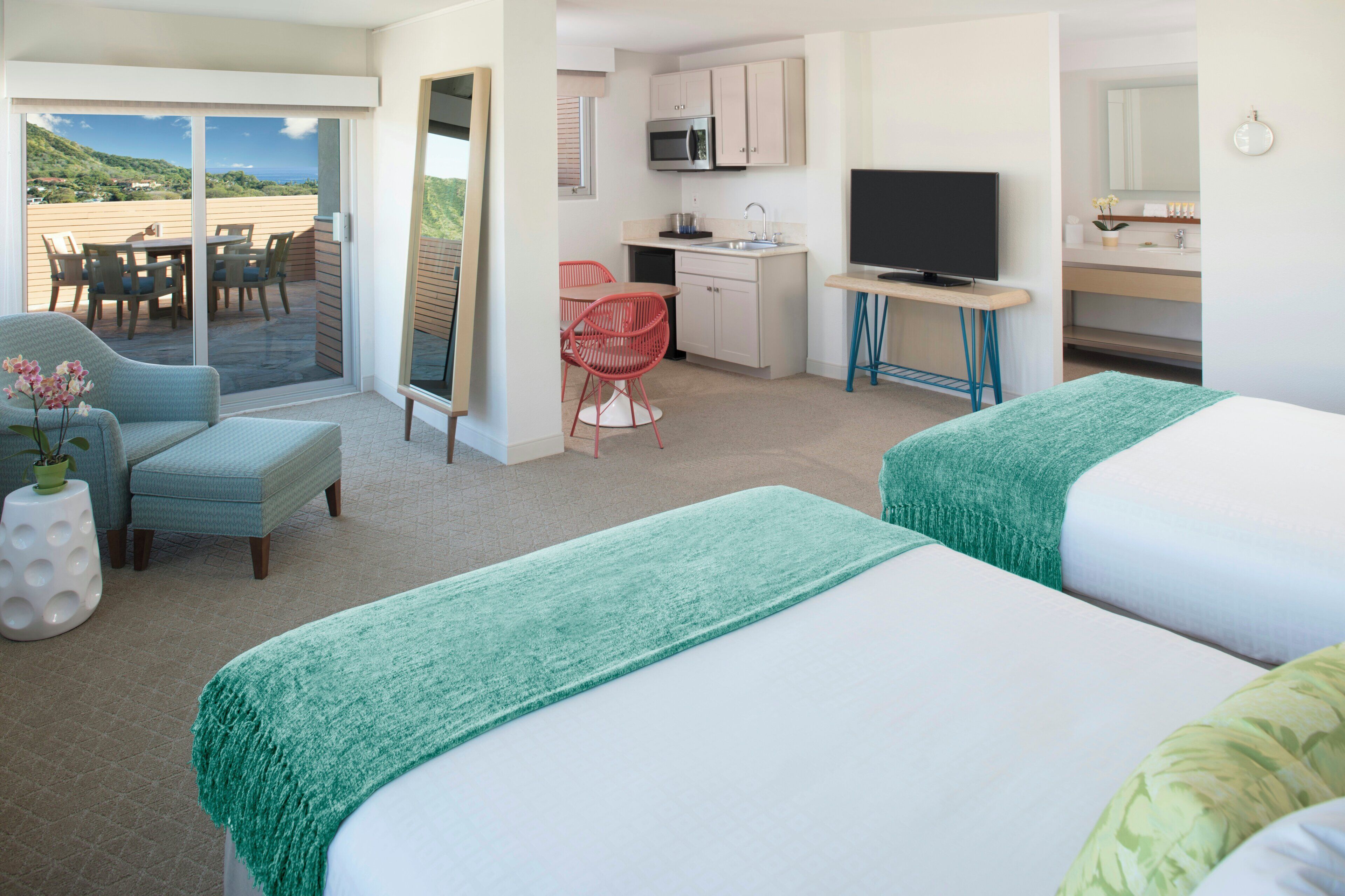 Ein Hotelzimmer mit zwei Betten, einem Essbereich, einer Küche und einem Fernseher.