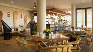 A restaurant with wooden furniture, a bar area, and large windows. - Queen Kapiolani Hotel (Honolulu)