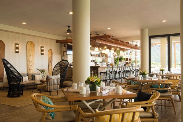 A restaurant with wooden furniture, a bar area, and large windows. - Queen Kapiolani Hotel (Honolulu)