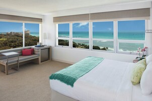 Ein Hotelzimmer mit Bett, Schreibtisch, Stuhl und großen Fenstern mit Blick auf das Meer und die Skyline.