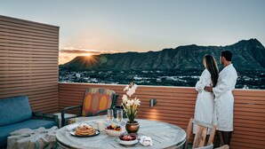 A couple on a balcony overlooking a mountain at sunset. - Queen Kapiolani Hotel (Honolulu)