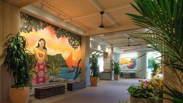 A lobby with a mural, potted plants, a reception desk, and a ceiling fan.