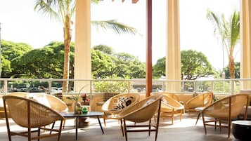 Un espacio de estar al aire libre cubierto, con sillas de mimbre y una mesa, con vistas a un estacionamiento y árboles.