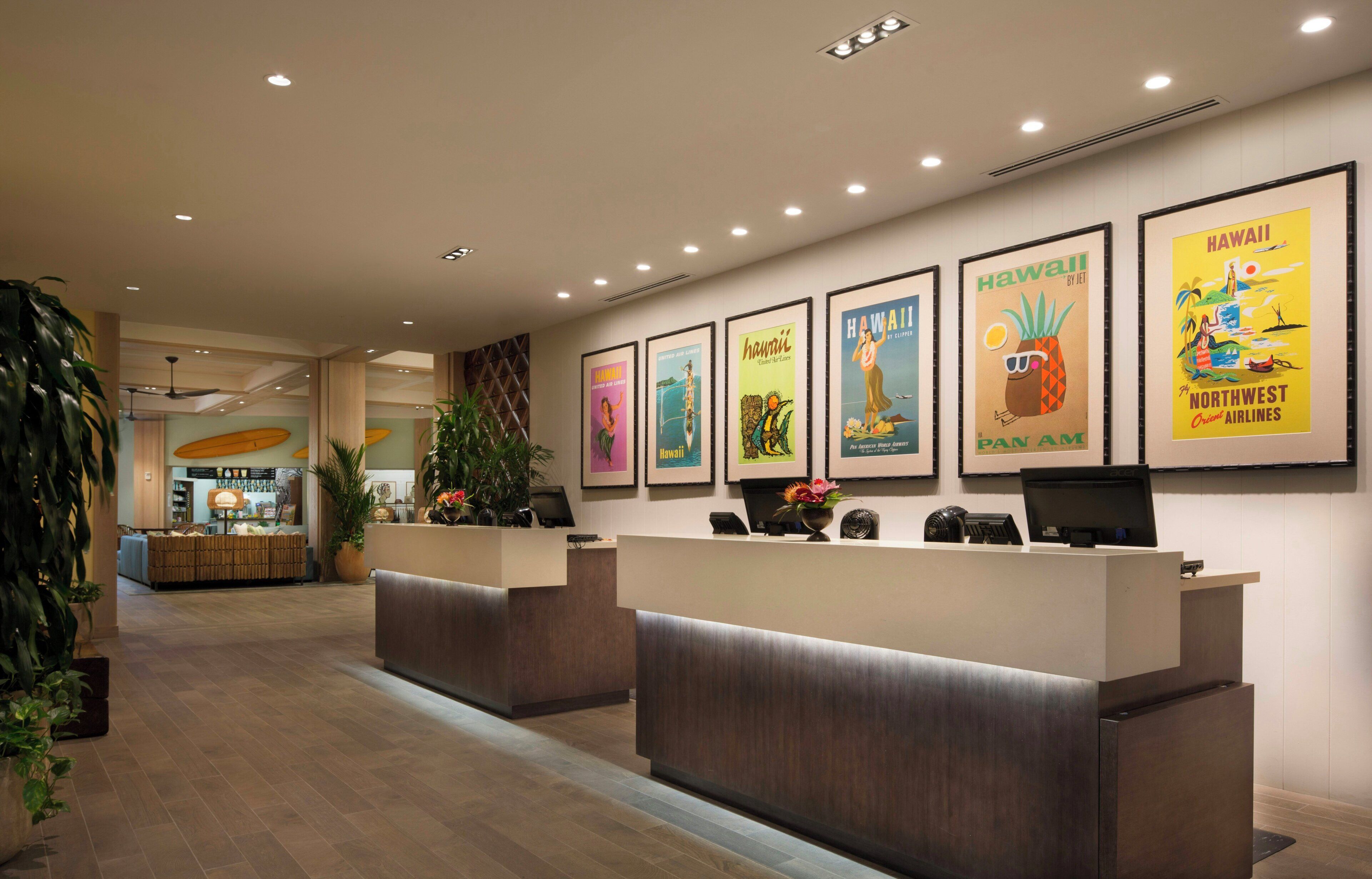 Zona de recepción de hotel con mostrador, carteles enmarcados y una planta.