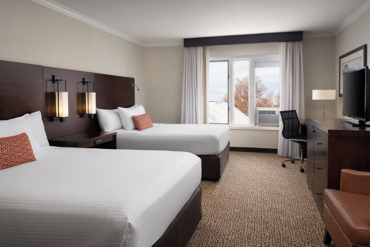 A hotel room with two beds, a desk, a chair, a TV, and a window with curtains.