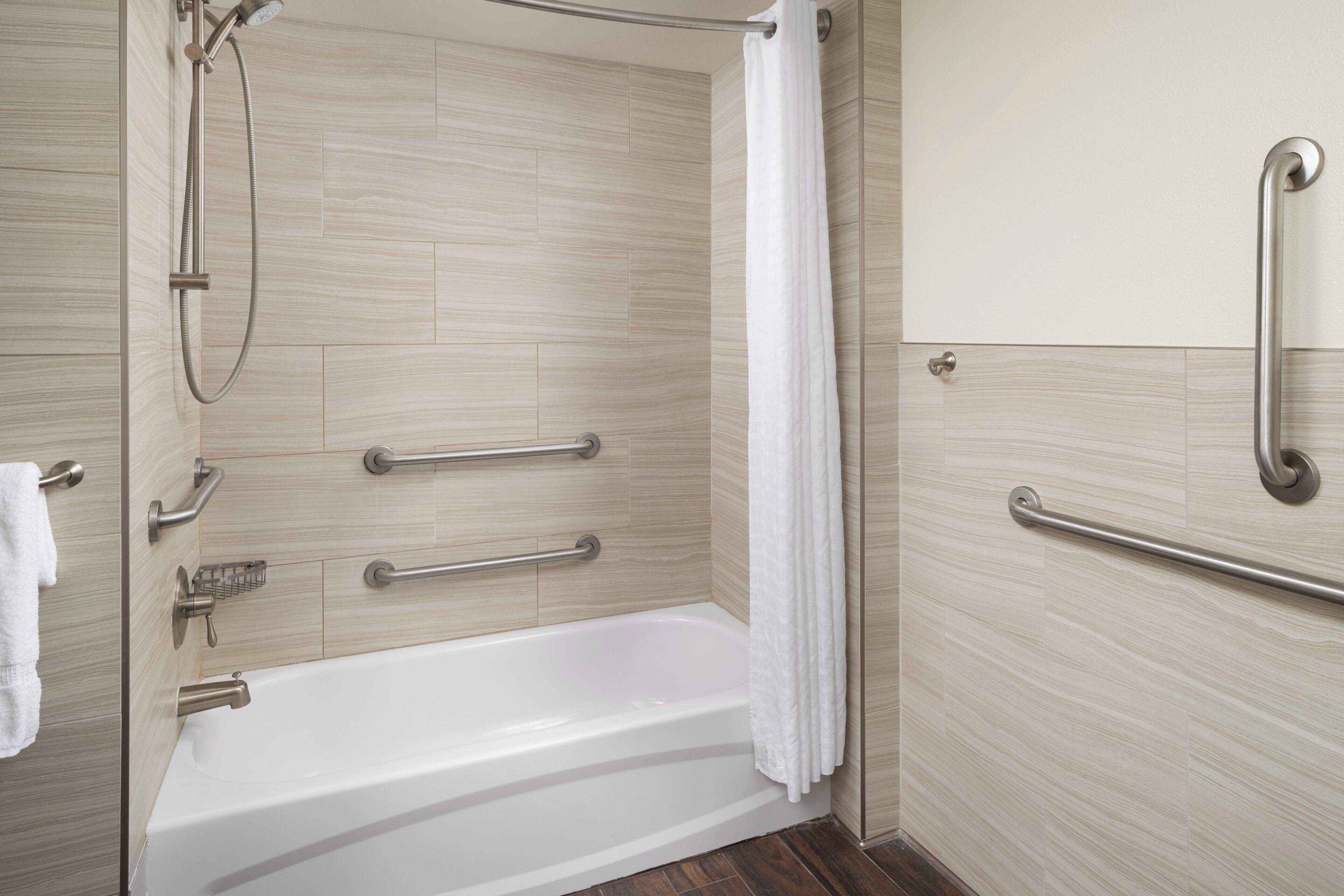 A modern bathroom with a bathtub, shower, and handrails.
